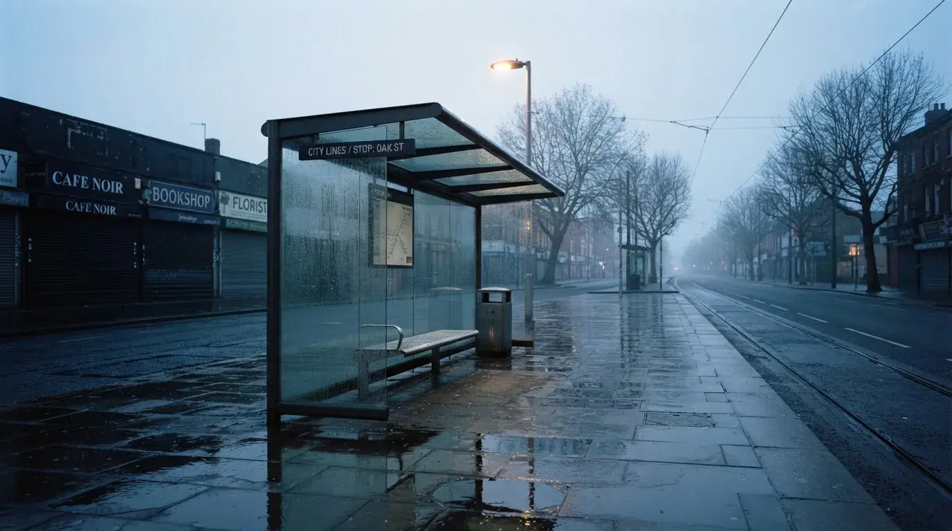 Pusta wiata przystanku tramwajowego na miejskiej ulicy o świcie, pusta ławka i mokry chodnik.